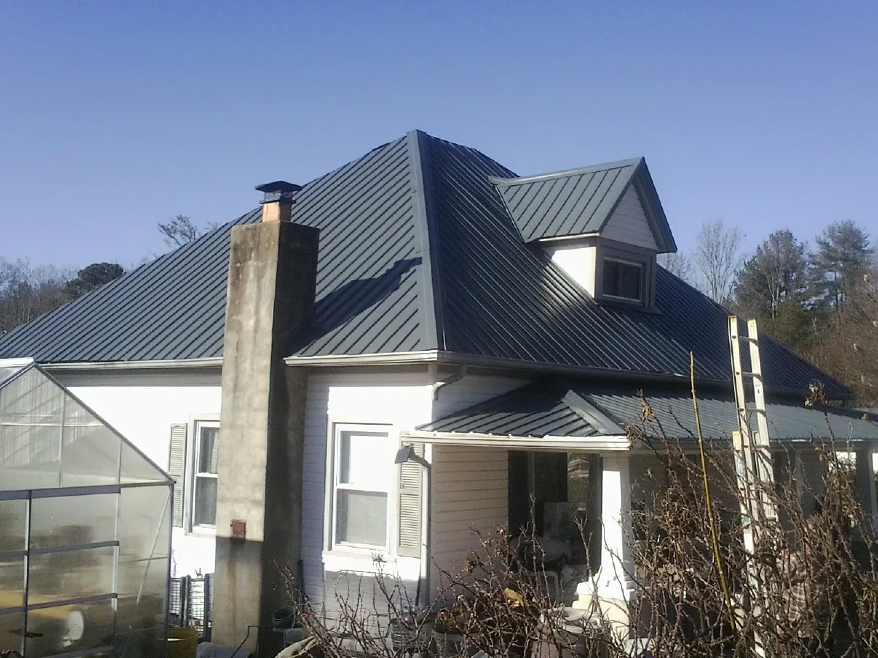 Dark blue standing seam metal roof on a white farmhouse with dormer — Slate & Tile Roof Repair by Roofing Brothers in Black Eagle
