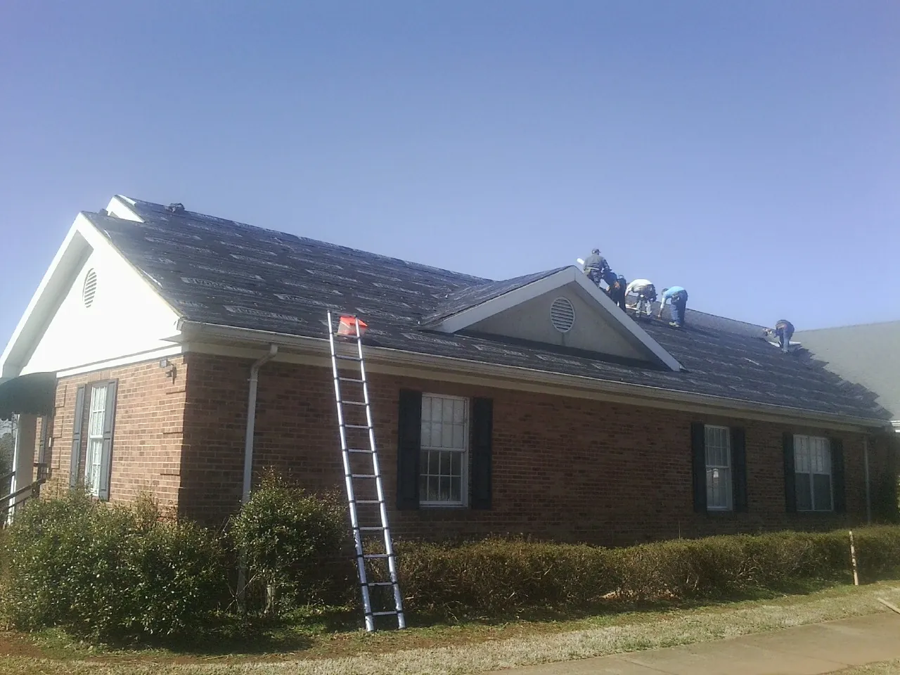 Crew tearing shingles off a brick ranch roof with a ladder set — Emergency Roof Repair work by our crew in Black Eagle