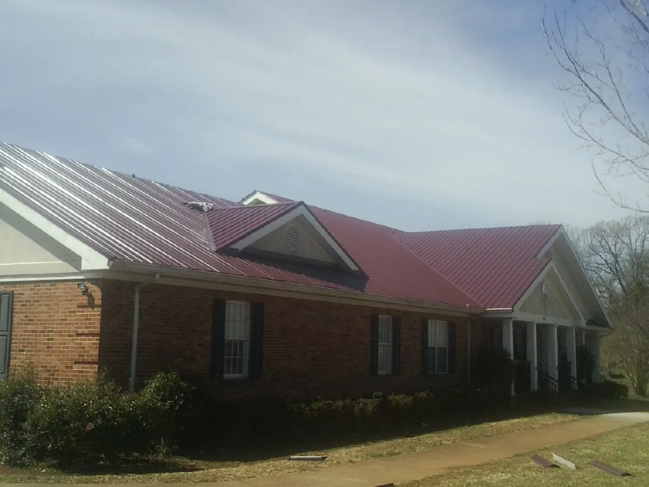 Red metal roof with gabled entries on a long brick building, from a Hail Damage Roof Repair job in Black Eagle