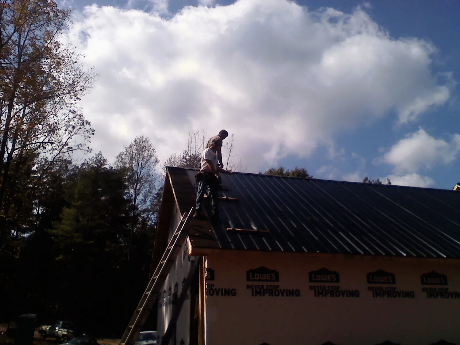 Roofer fastening dark metal panels high against a cloudy sky, from a Roof Inspection job in Black Eagle